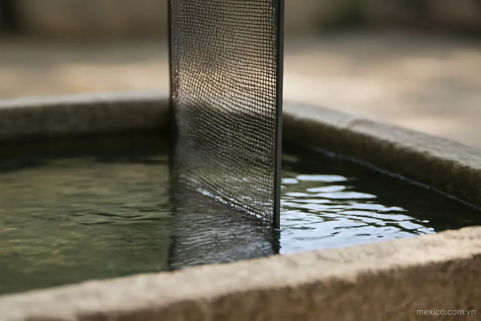A mesh screen dividing a shallow stone basin into two parts with different water levels, side view, no text