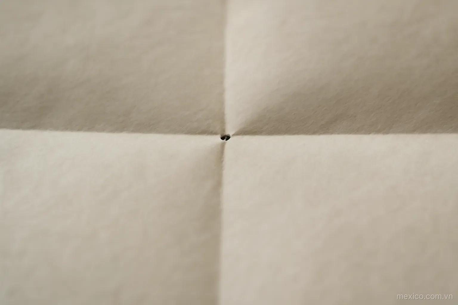 A single dot marked at the intersection of two crease lines on folded paper, close view, no text