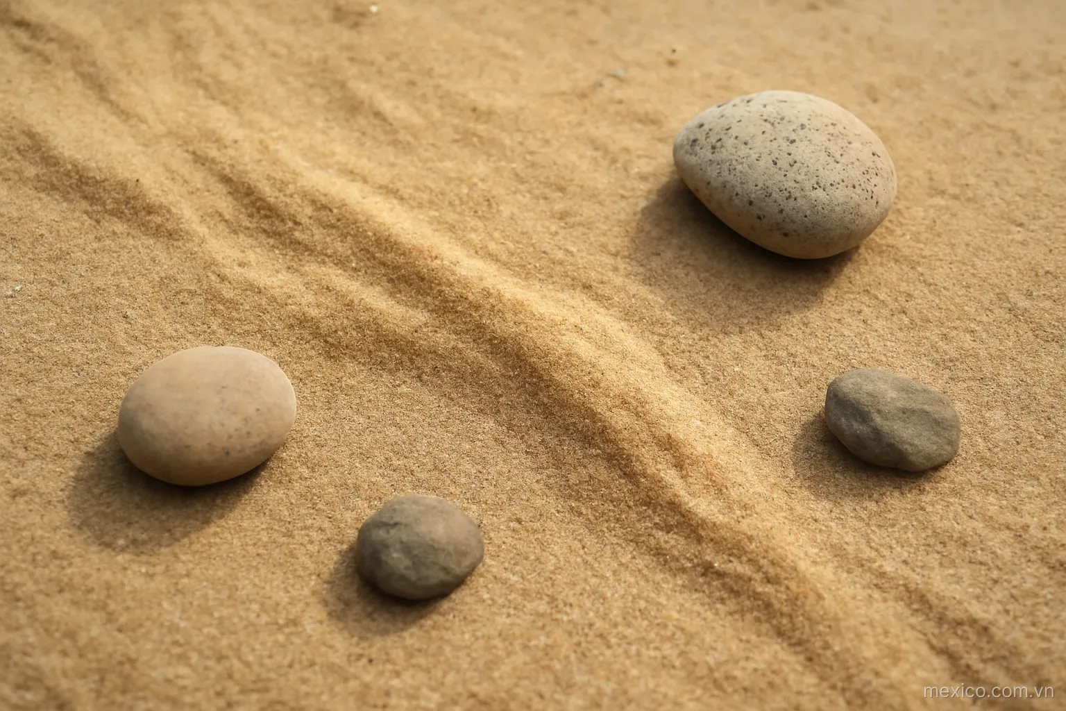 A stream of dry sand flowing across flat ground around a few fixed stones, overhead view, no text