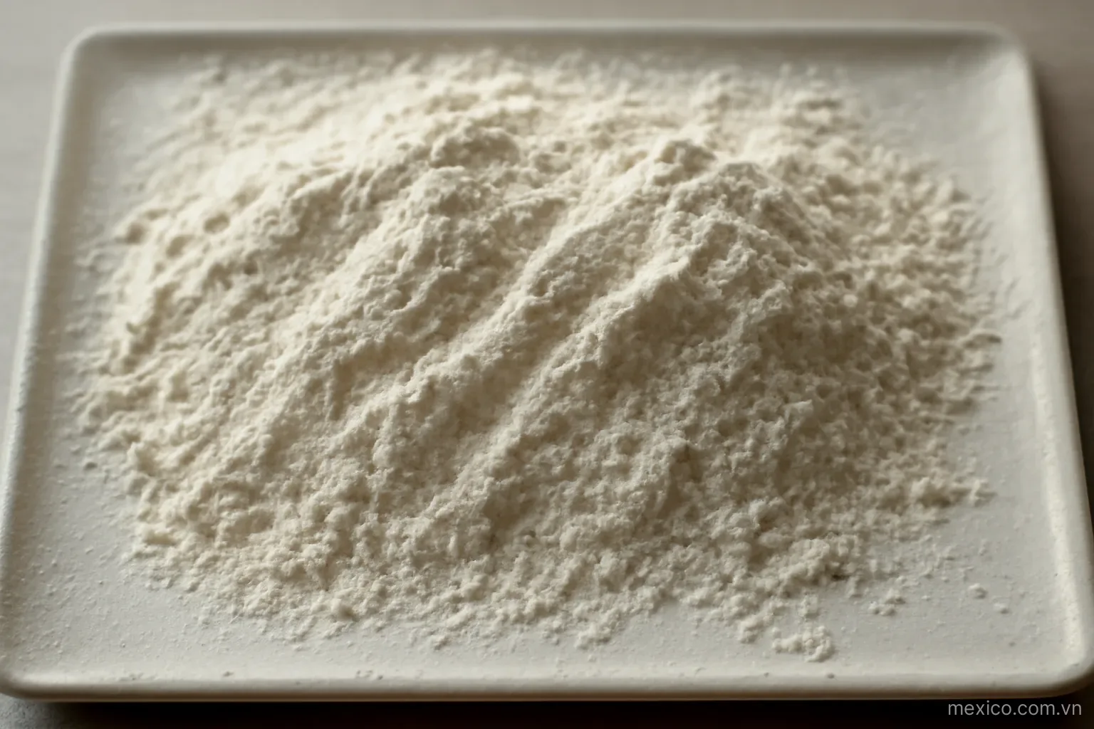 Fine powder scattered on a thin flat plate forming uneven ridges, overhead close view, no text