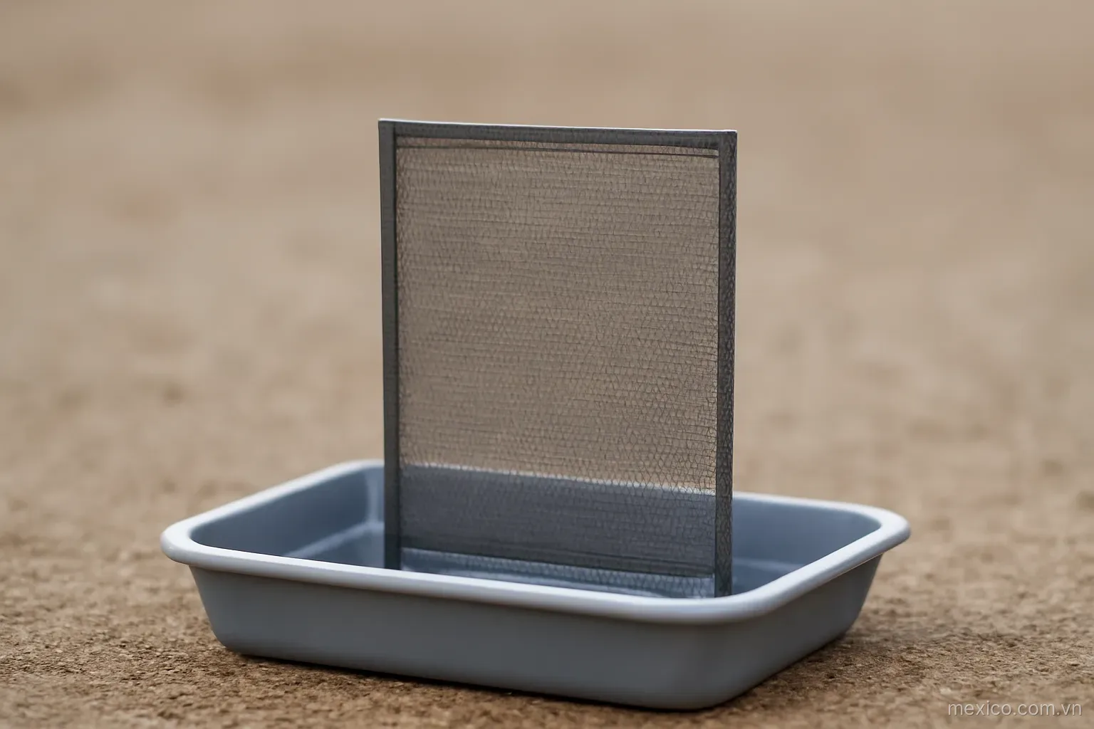 A fine mesh screen standing upright in a shallow tray of water, side view on plain ground, no text